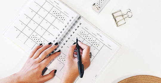 Zwei Hände mit einem Stift, die etwas in einen Kalender eintragen