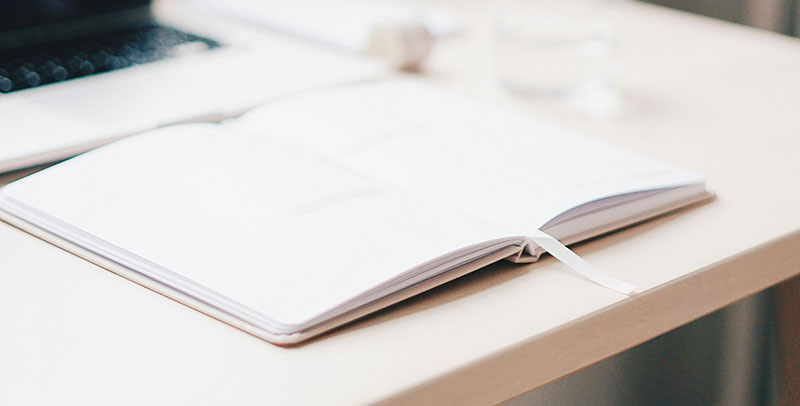 Ein aufgeklapptes Notizbuch vor einem Laptop auf einem Tisch